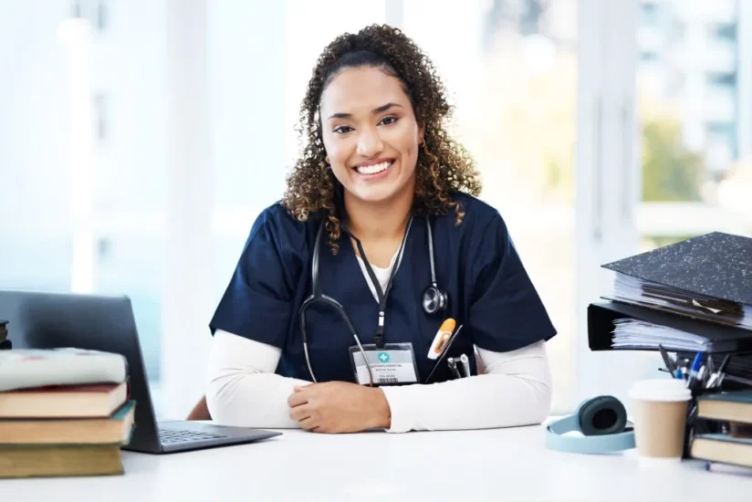 Nursing student in scrubs sitting at a desk with a stethoscope, smiling confidently in a classroom setting